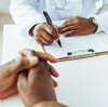 A close up of a man with his hands crossed on the table as he sits across from his doctor who is taking notes. Talking to your doctor can be confusing, but a few tips can help you create the partnership that you need to support your health.