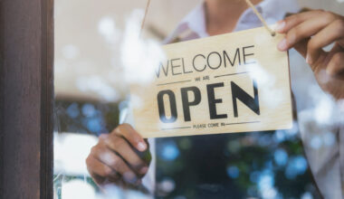 A person hanging a sighn that reads: open.