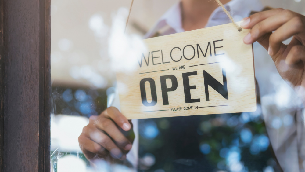 A person hanging a sighn that reads: open.