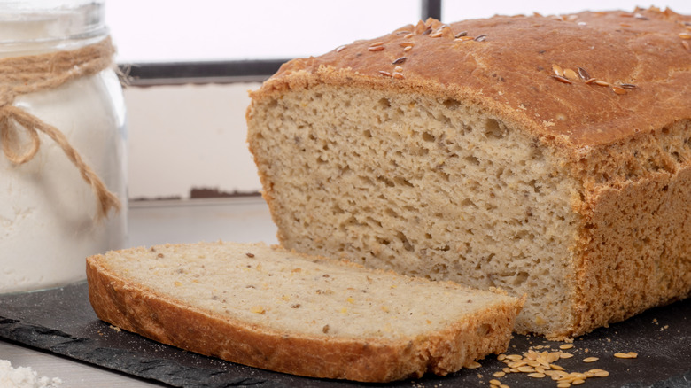 A loaf of bread with one slice sitting on a slate cutting board