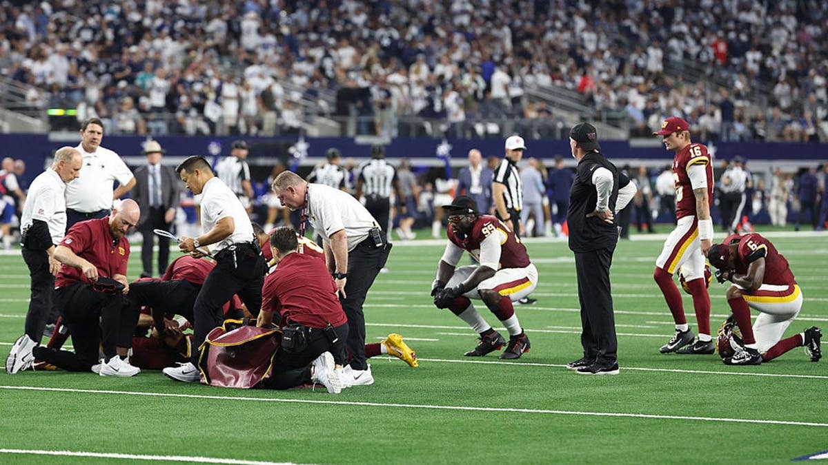 Jayden Daniels #5 lies on the field as medical staff attend to him during a game.