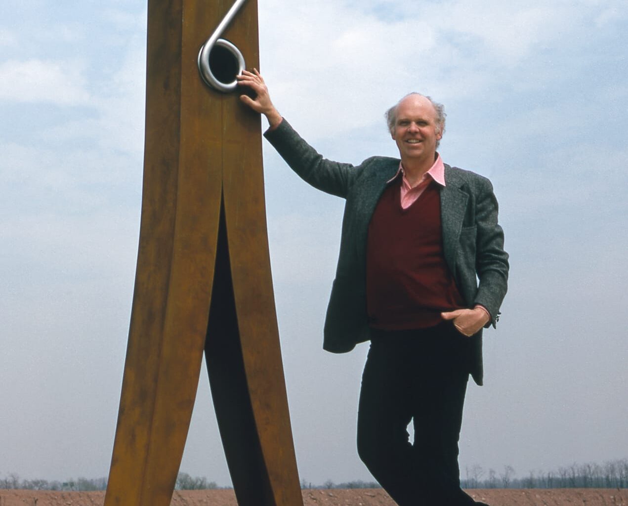 a historical photograph of artist Claes Oldenburg standing beside a giant, 10-foot clothespin sculpture