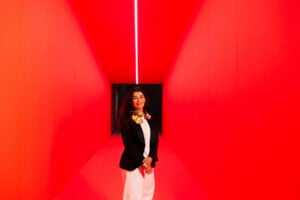 Es Devlin standing inside a vivid red, angular corridor