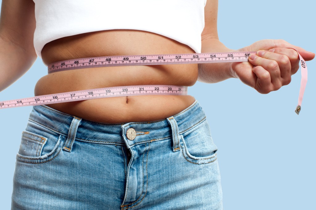 An overweight woman wraps a tape measure around her waist.