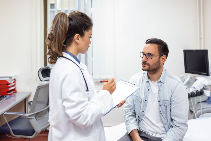 A female doctor taking notes on a clipboard while talking to a male patient.