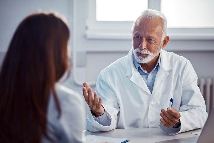 Elderly male doctor speaking dismissively to a patient in an office, illustrating bad experiences with doctors