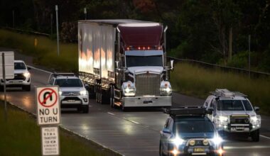A large semi-trailer truck travels along a multi-lane road alongside several passenger and utility vehicles.