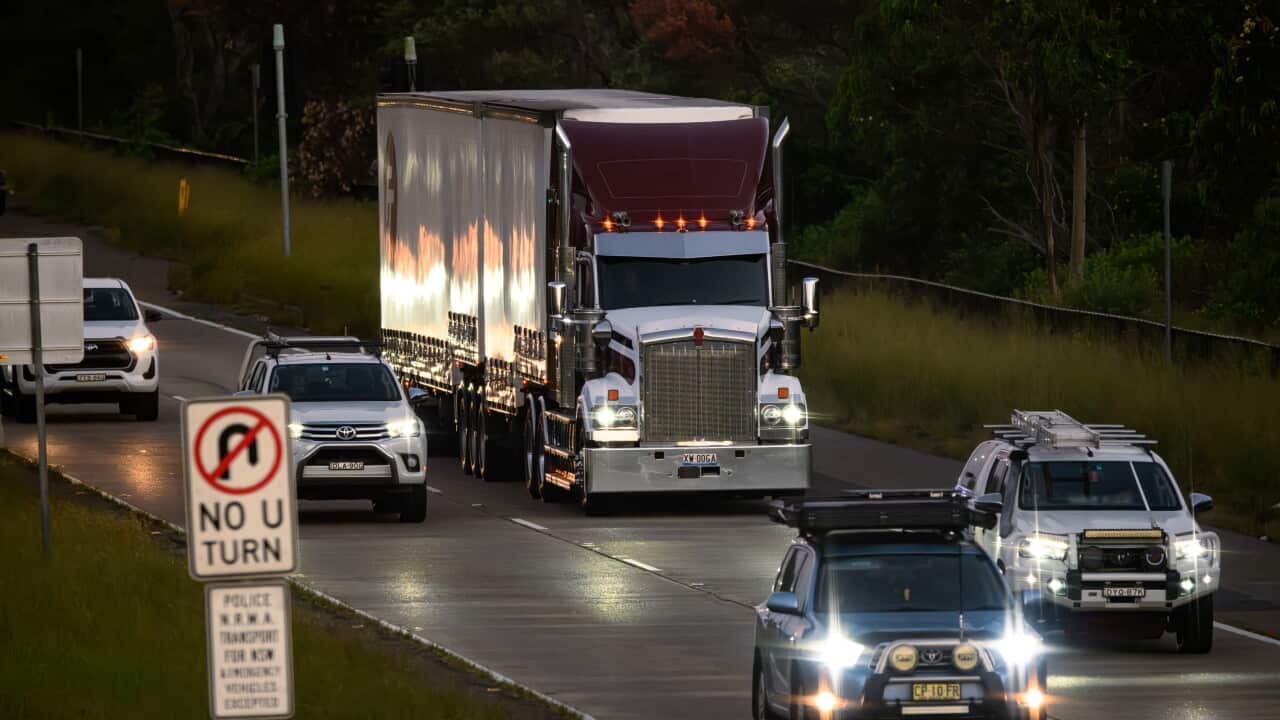 A large semi-trailer truck travels along a multi-lane road alongside several passenger and utility vehicles.