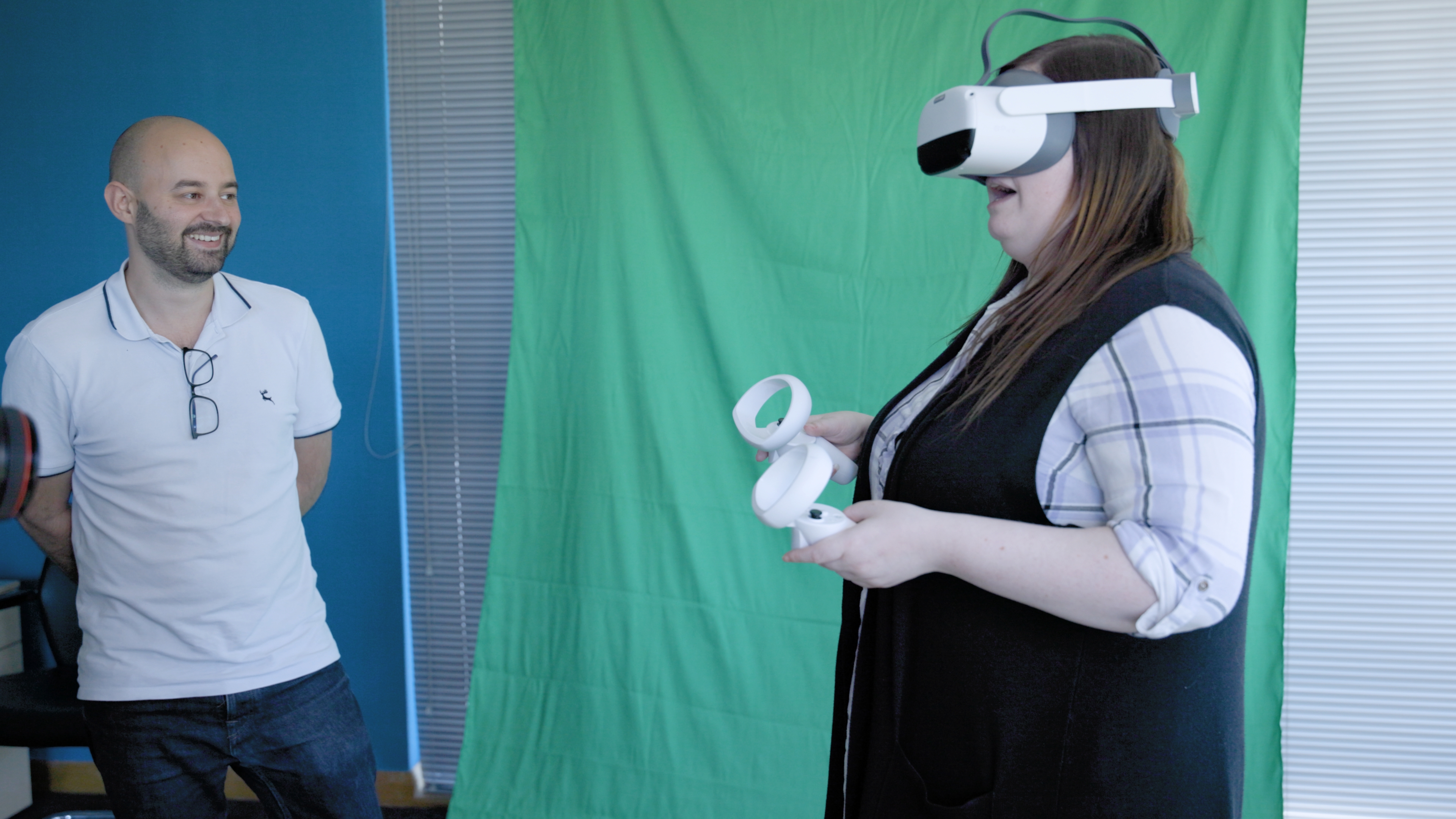 Woman using a VR headset and controllers, observed by a man.
