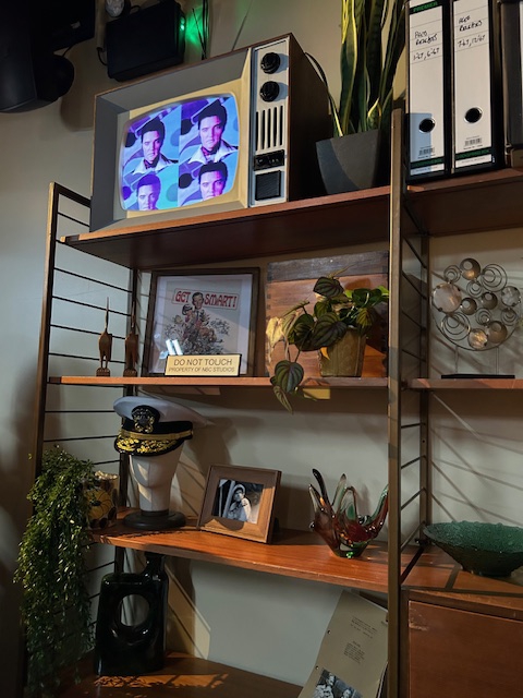Prop shelf with vintage television showing Elvis Presley, plants, and memorabilia.