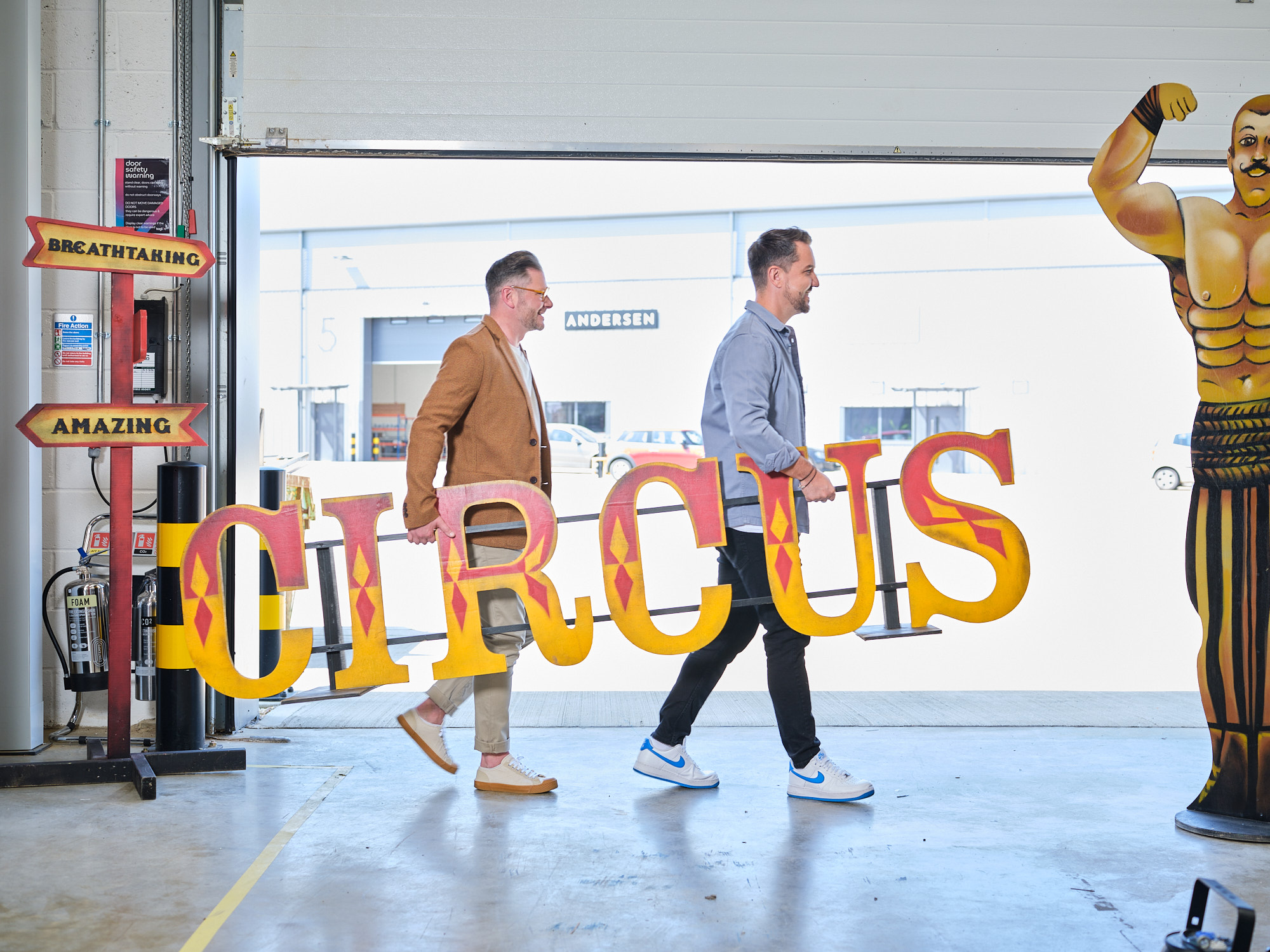 Two men carrying a large circus sign.