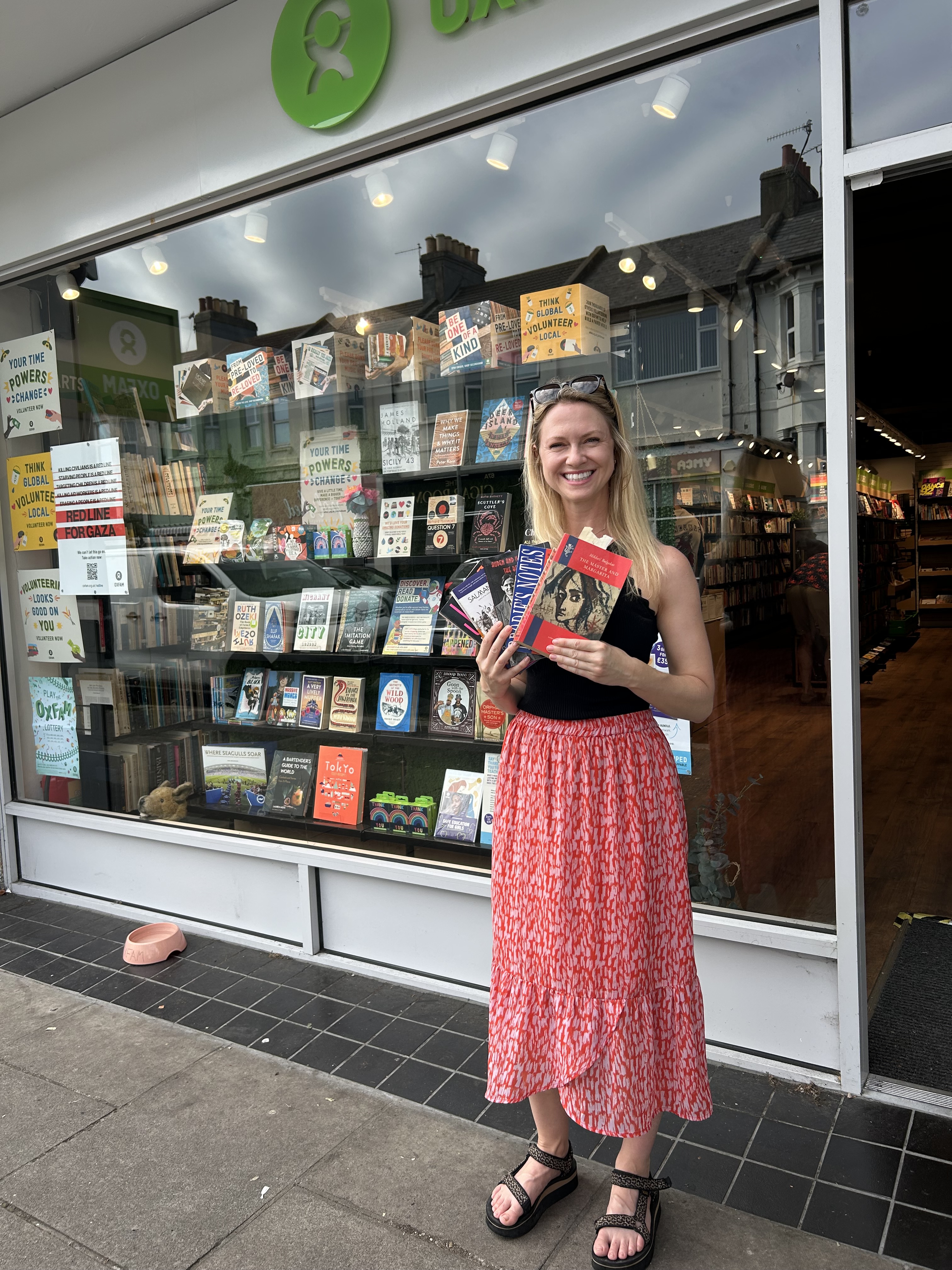 Woman holding books in front of an Oxfam bookstore.