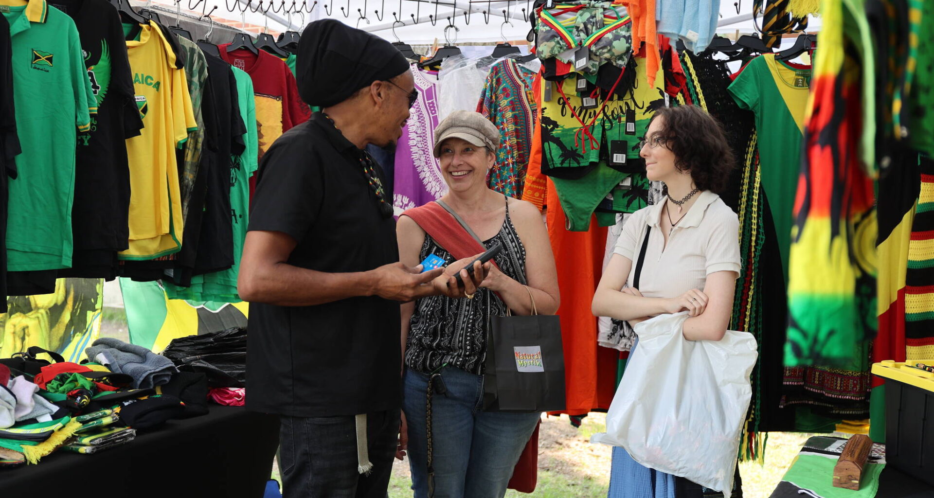 Warren Benns (left), owner of Natural Mystic shares a laugh with Stacey (middle) and Izzy Eaton at the Naija Market in Princess Park Saturday afternoon in downtown Brandon. (Michele McDougall/The Brandon Sun)