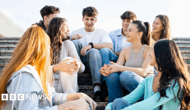 Eight young people sitting on steps outside on what looks a sunny day. Three are male and five are female