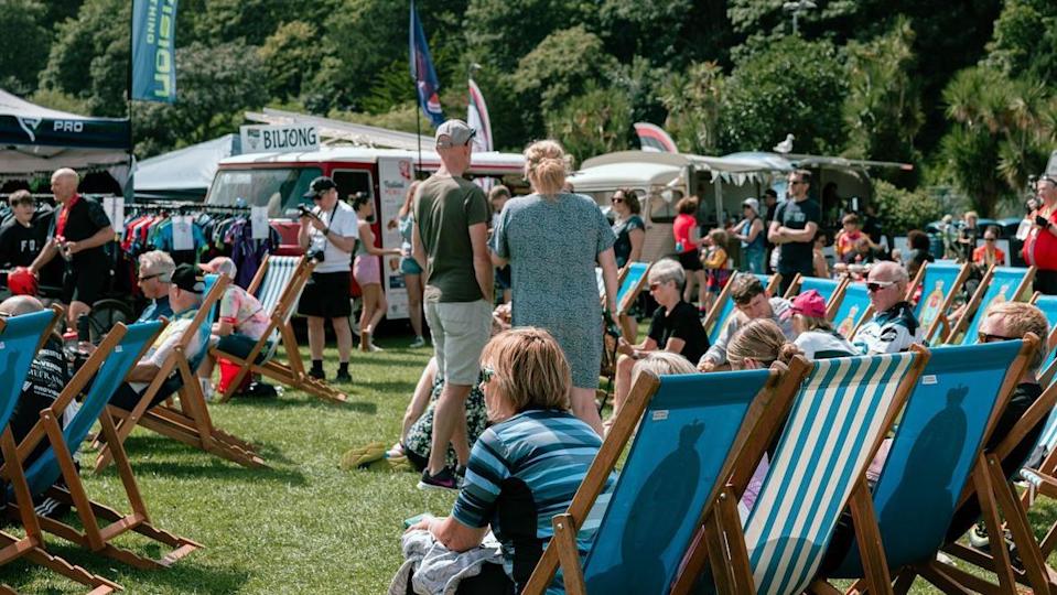 Crowds of people in the Mooragh Park in Ramsey. Many are sitting on blue deckchairs and there are food stalls and vans in the background.