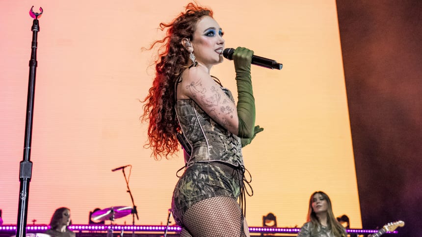A singer with red hair and an outfit made of camouflage material holds onto a microphone.
