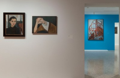 Two paintings of a woman hanging on a white wall. Visible through a portal is a blue wall hung with an abstract painting resembling machinery.