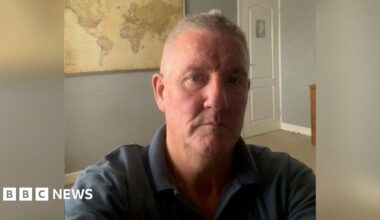 A selfie of Mark Hemphill, he is indoors wearing a navy polo shirt. A world map is on the wall behind him.