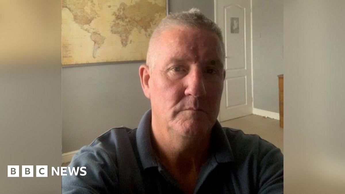 A selfie of Mark Hemphill, he is indoors wearing a navy polo shirt. A world map is on the wall behind him.