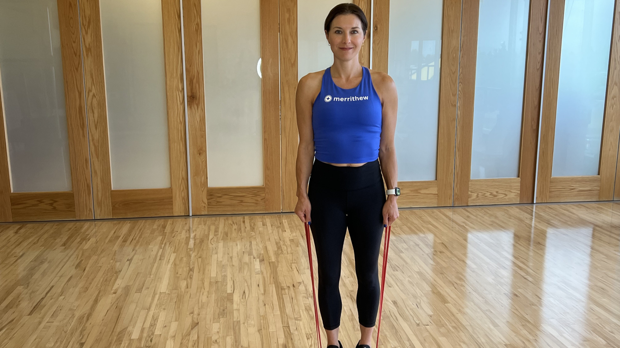 Woman demonstrates exercise using resistance band in fitness studio