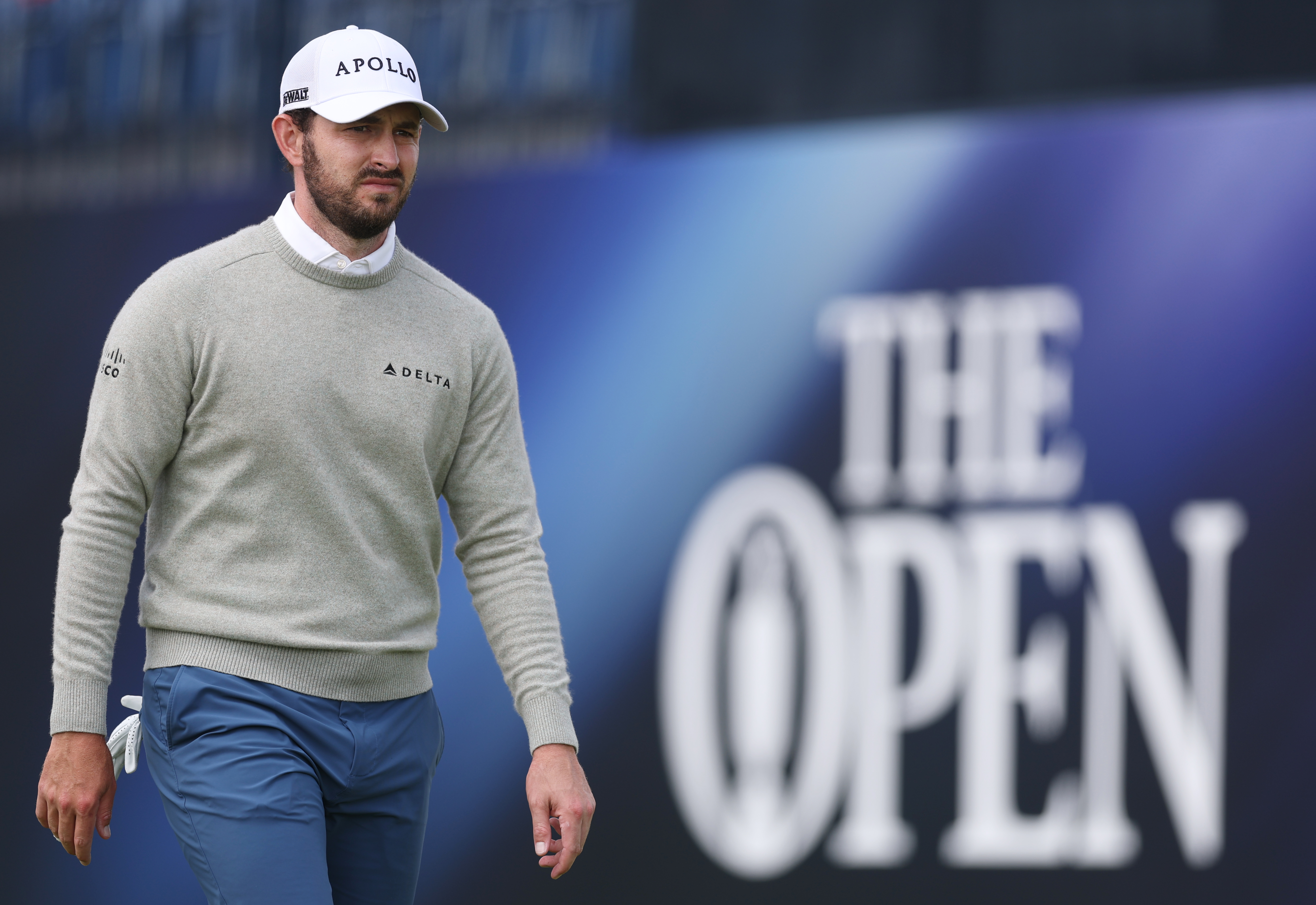 Patrick Cantlay walks in front of an Open Championship banner