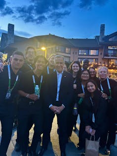 A group of young adults stand smiling with a middle-aged man in a suit
