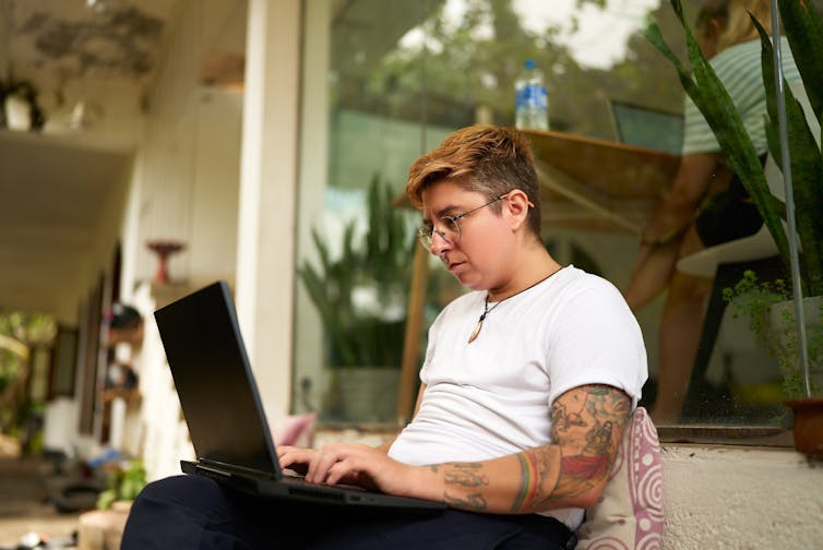 A young adult with short hair wearing glasses types on a laptop