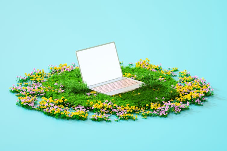 An open laptop resting on green grass, surrounded by yellow and pink flowers.