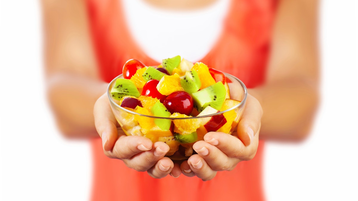 Healthy mix fruit salad, closeup on fresh summer dessert, woman holds lunch bowl.