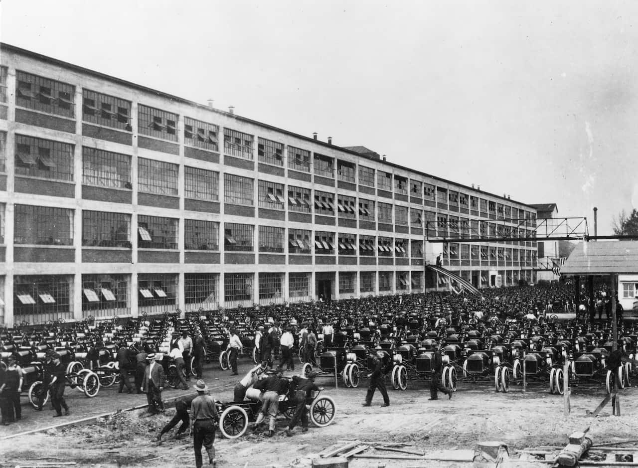 A black and white photo shows Model T Ford cars lined up outside a warehouse building.