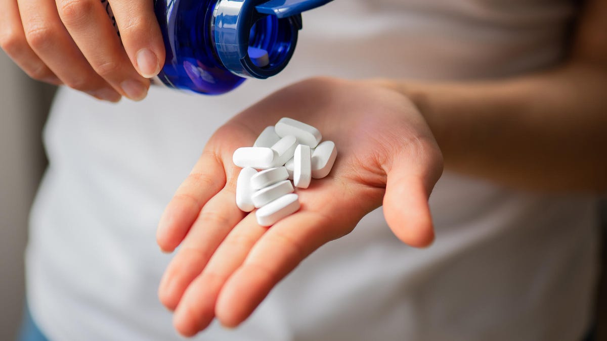 A person pouring white pills into their hand out of a blue pill bottle.