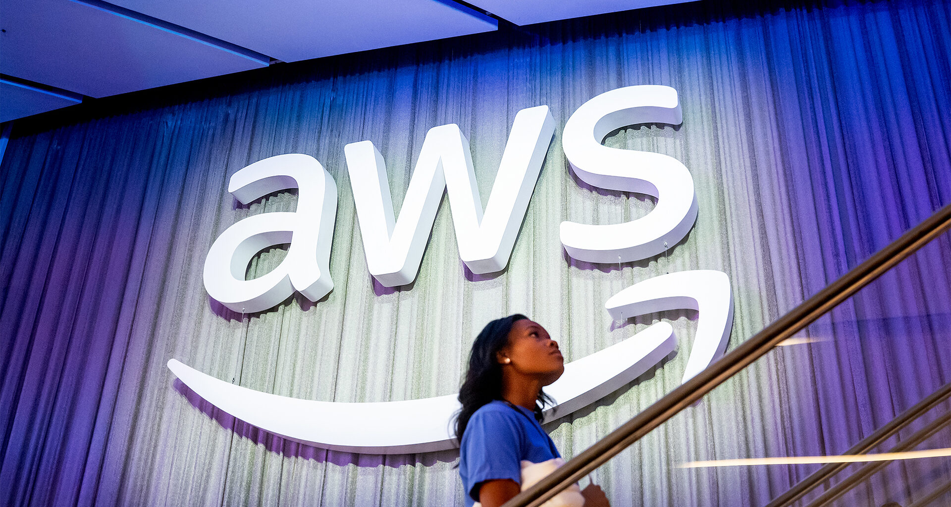 AWS logo and branding pictured at the AWS re:Invent conference at the Venetian Hotel and Casino in Las Vegas, US, with a woman walking up stairs in foreground.