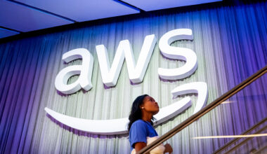 AWS logo and branding pictured at the AWS re:Invent conference at the Venetian Hotel and Casino in Las Vegas, US, with a woman walking up stairs in foreground.