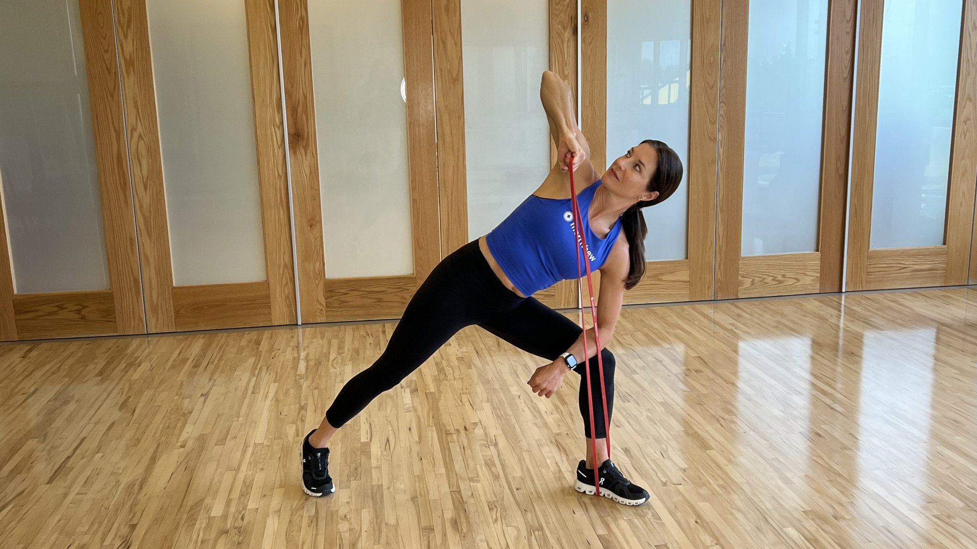 Woman demonstrates exercise using resistance band in fitness studio
