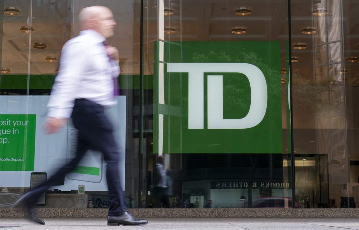 A blurred man walks past the TD Bank symbol on a glass window. 