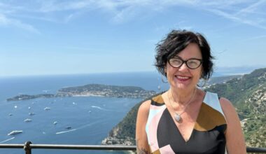 A smiling, middle-aged woman posing atop a hill with views of a waterway in the background.