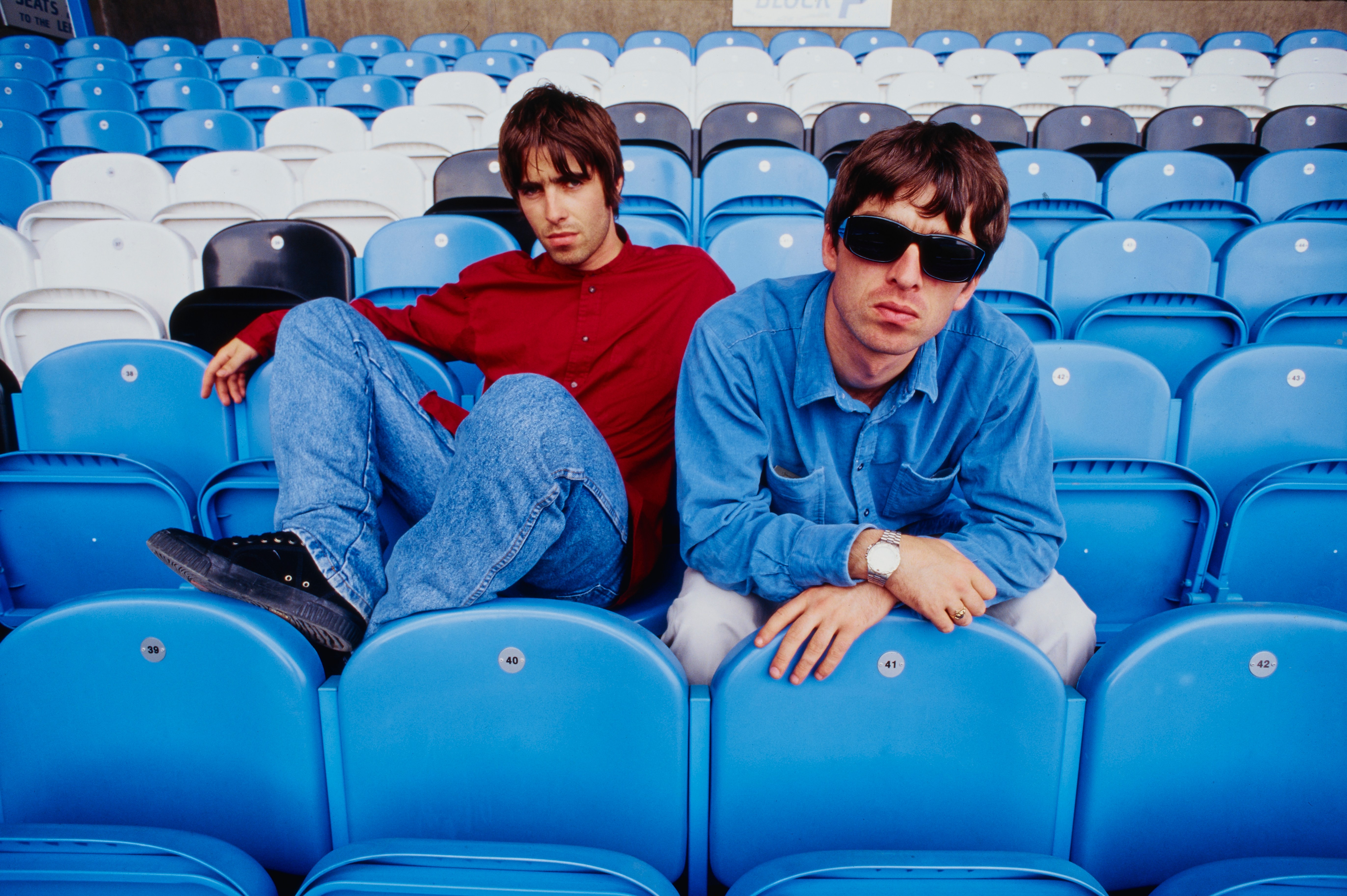 Liam and Noel Gallagher of Oasis sitting in stadium seats.