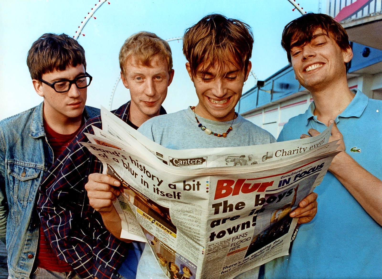 Blur band members reading a newspaper article about themselves.