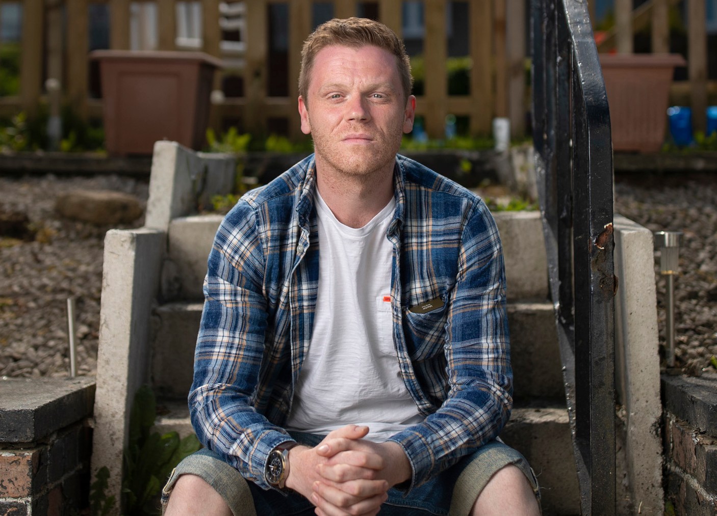 Portrait of Darren McGarvey (AKA Loki), sitting on steps outside his home.