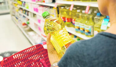 A shopper holds a clear plastic container of golden vegetable oil in her hand and looks at it in the aisle of a grocery store.