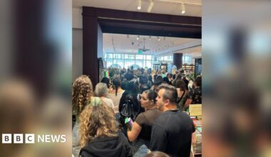 A picture inside a large bookshop at the back of a large crowd, which stretches to the far, windowed wall.