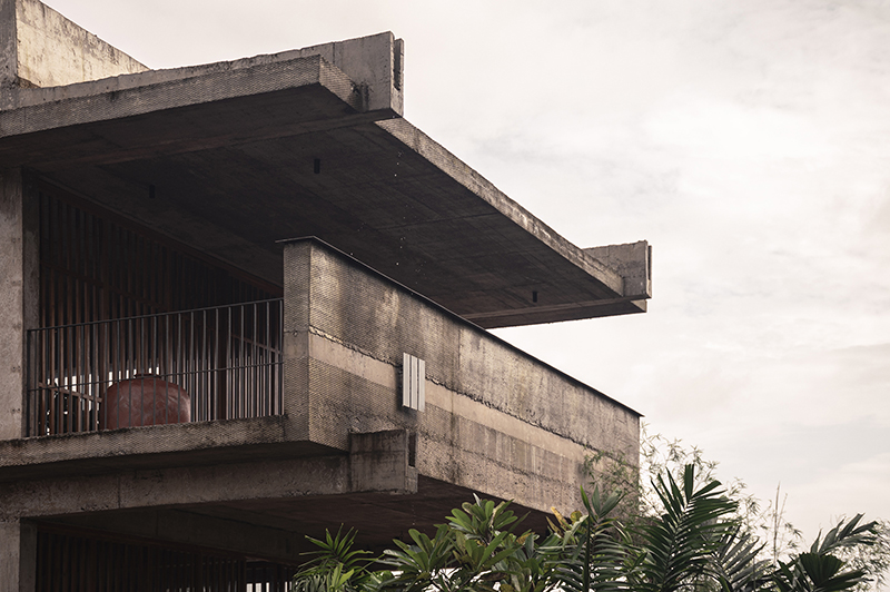 hybrid office-residence extends raw concrete balcony above recessed timber mass in india