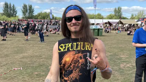 BBC Man with long brown hair wearing rock music vest and sunglasses