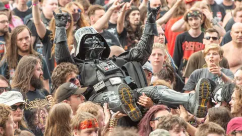 Getty Images A person dressed in a black Darth Vader costume with helmet and gloves crowd surfs over people at a heavy metal music festival.
