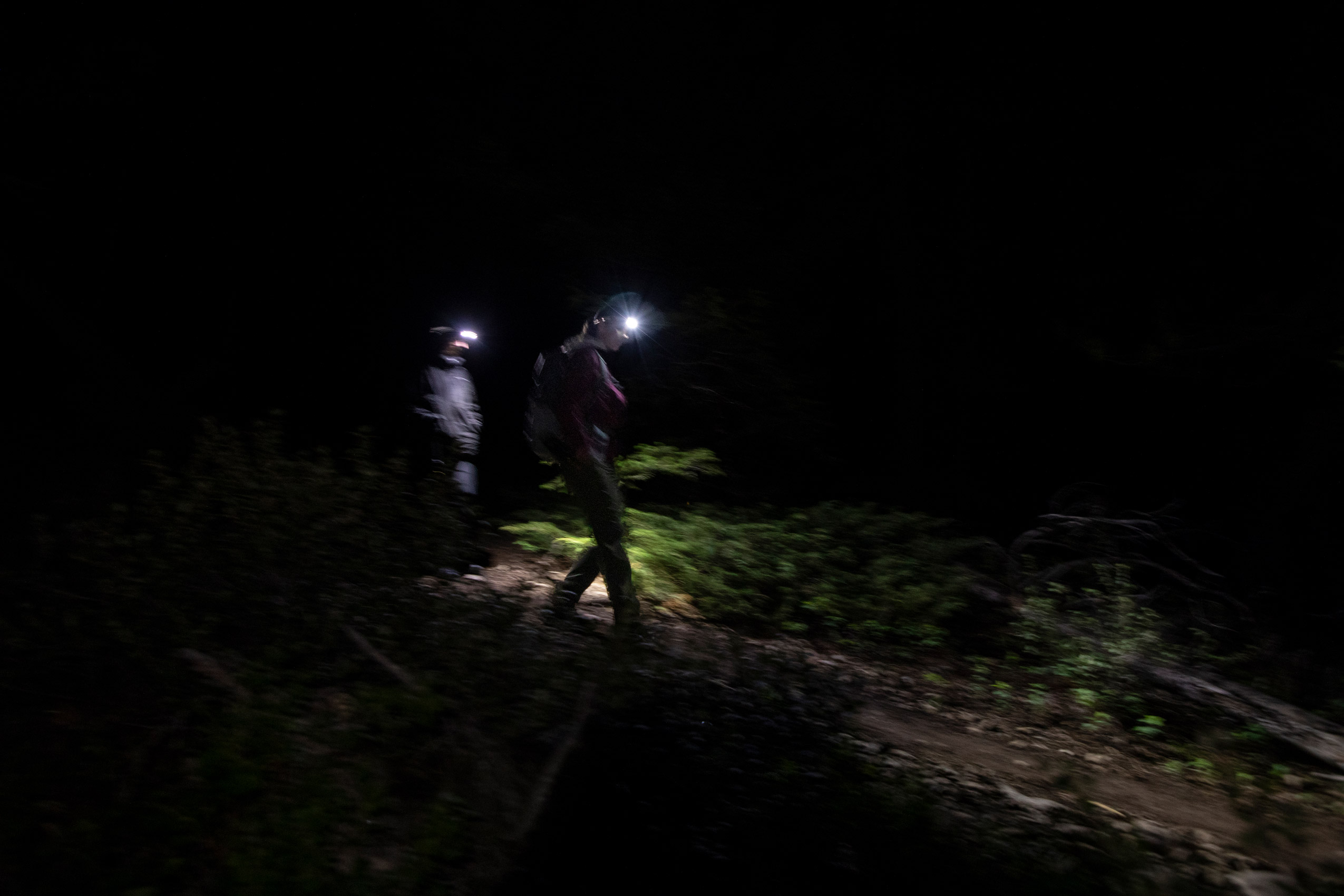 Two hikers with headlamps walk down a trail in the dark