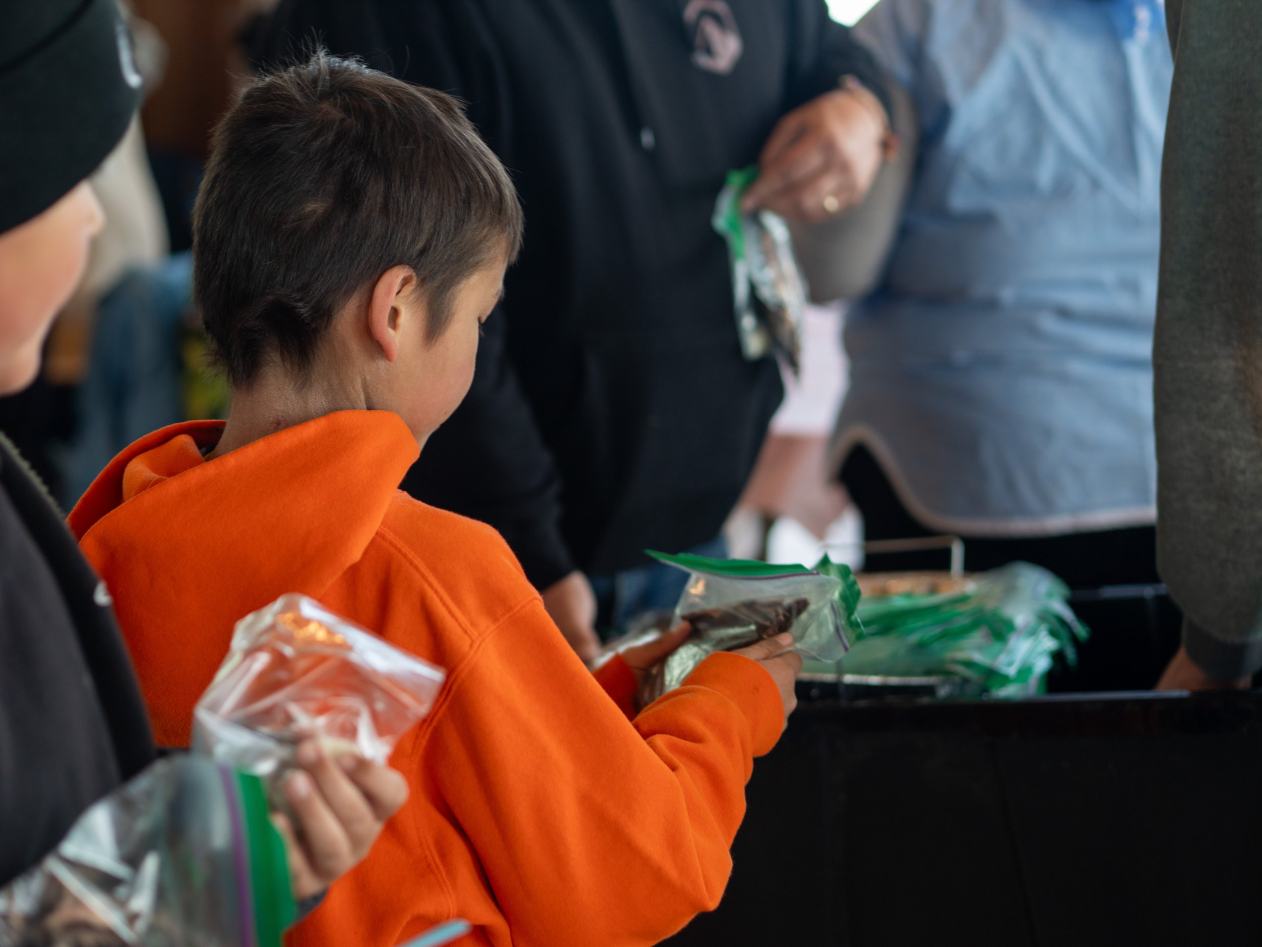 A child in an orange hoodie holds a plastic baggie full of dried caribou meat during the Caribou Days festivities in Old Crow, Yukon.