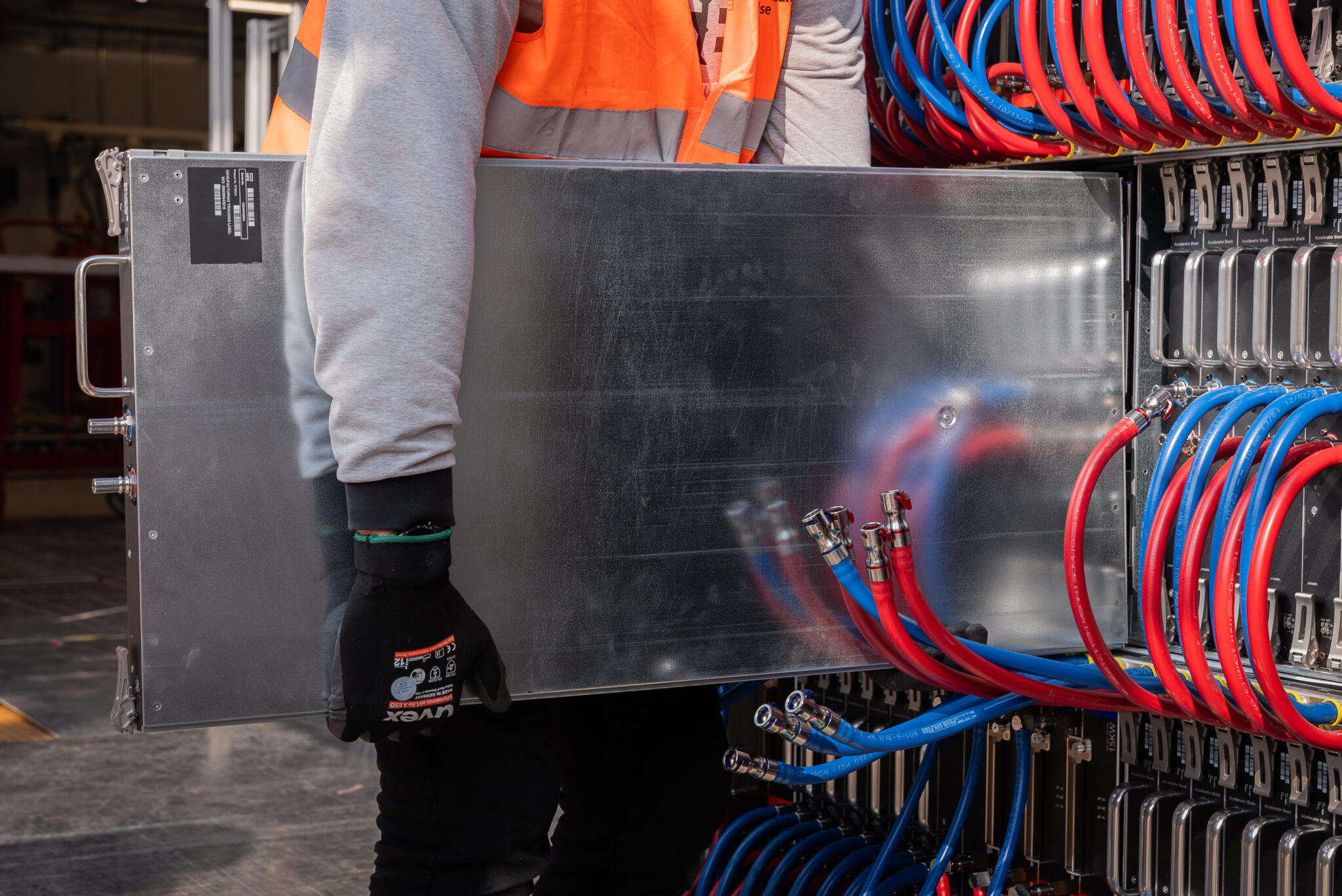 A technician carefully installs a server blade equipped with direct liquid cooling, demonstrating the hands-on precision involved in assembling Isambard-AI’s advanced computing infrastructure.
