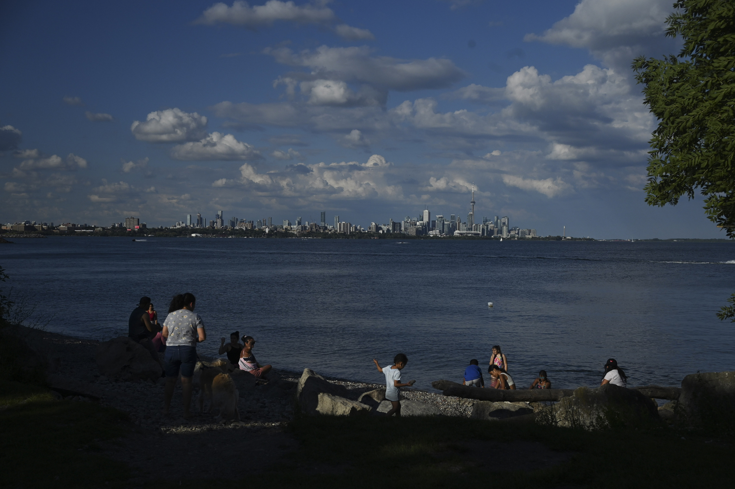 Mimico Creek spill: families hang out on a rocky beach on a summer day with Lake Ontario and the Toronto skyline behind them
