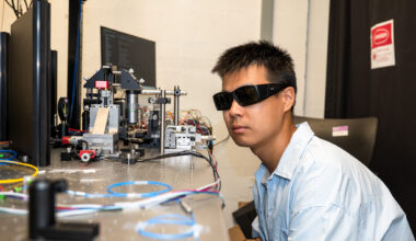 A scientist wearing goggles looks at a wire.