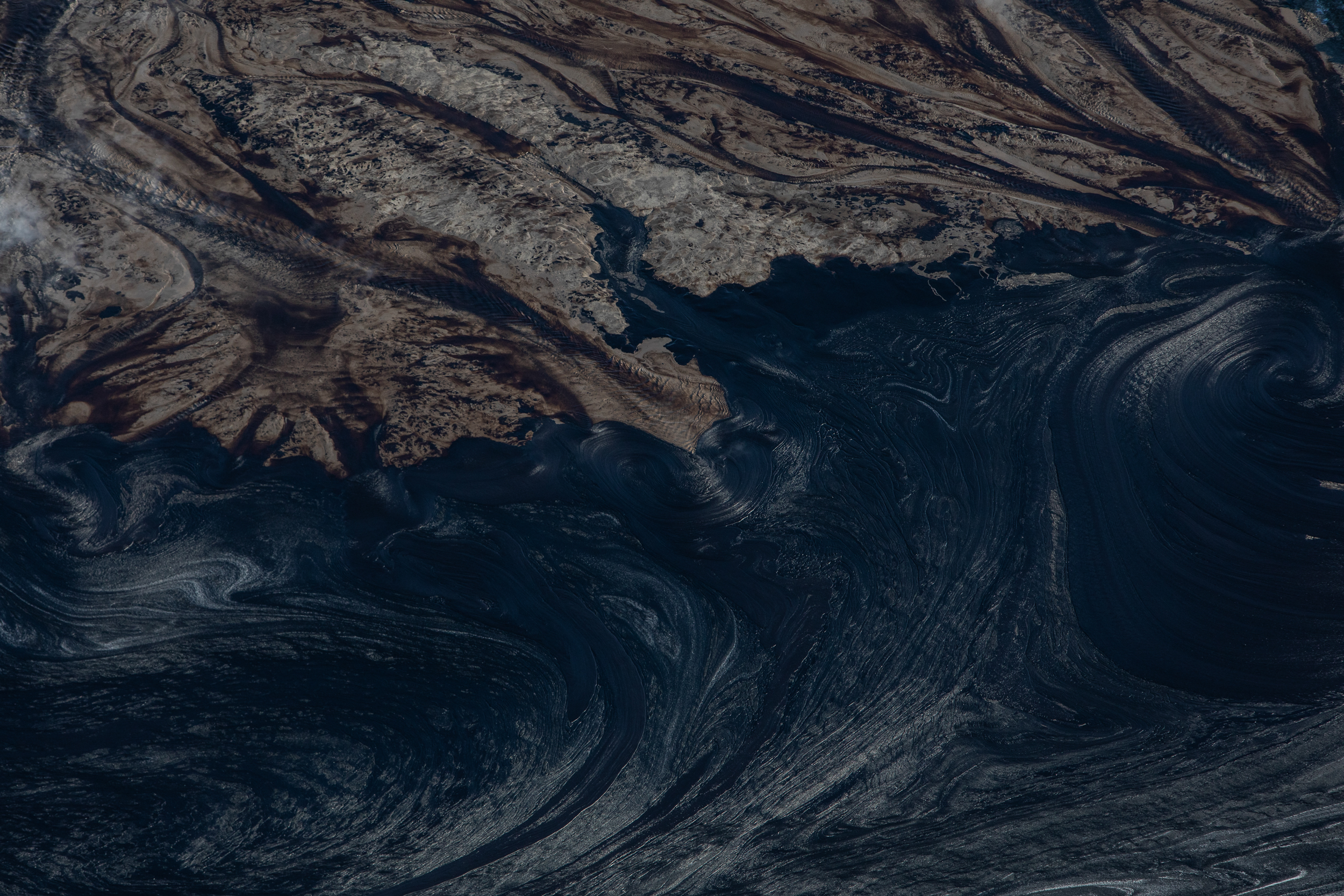 Inky black liquid meets brown in a tailings pond at a Suncor open pit oilsands mine